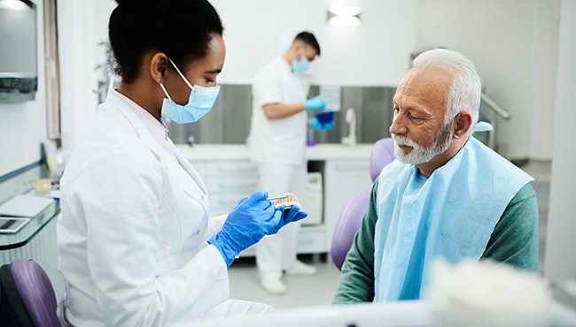 A dentist showing dentures to her older male patient