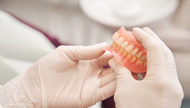 A closeup of gloved hands holding a denture